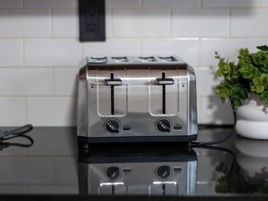 A stainless steel toaster on a black countertop with a white tiled backsplash and a potted plant to the right. - Beautiful 2BR Home, Near NYC, PATH & Lincoln Park (Jersey City)