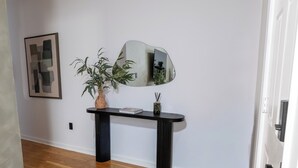 Een hal met een houten vloer, een zwarte consoles en een vaas en een boek, een spiegel, en een lijst met abstracte kunst aan de muur.