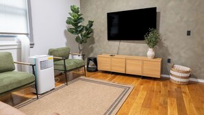 Een woonkamer met een bank, een televisie, een plant, een radiator en een houten kast.