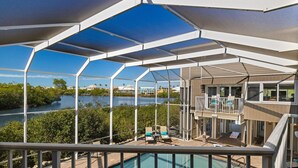 A poolside area with a view of a river, a covered deck, and a building with a balcony. - Widgeon Point (Fort Myers Beach)