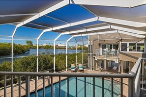 A poolside area with a view of a river, a covered deck, and a building with a balcony. - Widgeon Point (Fort Myers Beach)