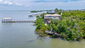 A coastal house with a dock extending into the water, surrounded by lush greenery. - Widgeon Point (Fort Myers Beach)