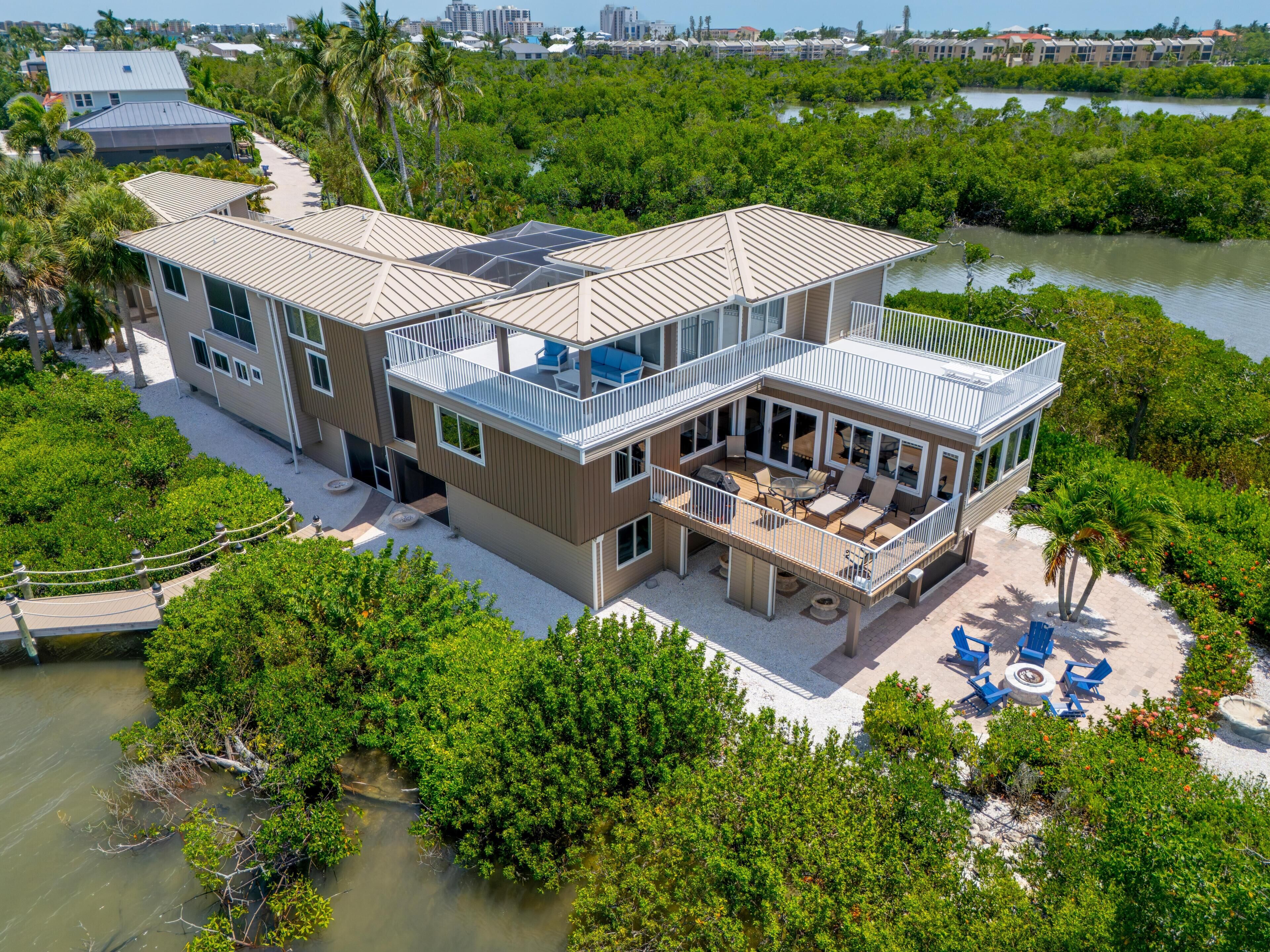 A modern multi-story house with a large deck, surrounded by dense mangrove vegetation and a body of water.