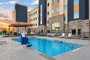 A swimming pool with a lifeguard stand, lounge chairs, and a stone building with multiple windows.