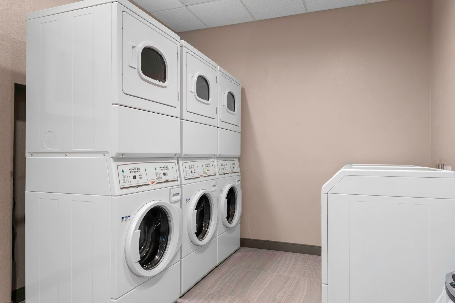 A laundry room with stacked washers and dryers, a beige wall, and a tiled floor.