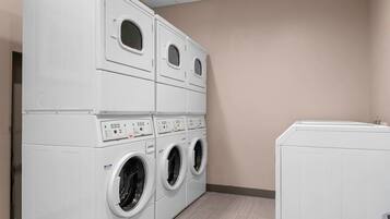 A laundry room with stacked washers and dryers, a beige wall, and a tiled floor.