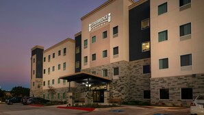 A Staybridge Suites hotel with a modern design, featuring a stone facade, multiple windows, and a covered entrance.