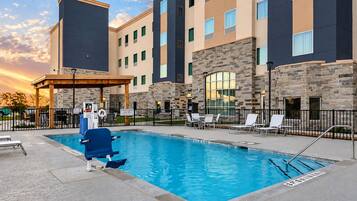 A swimming pool with a lifeguard stand, lounge chairs, and a stone building with multiple windows.