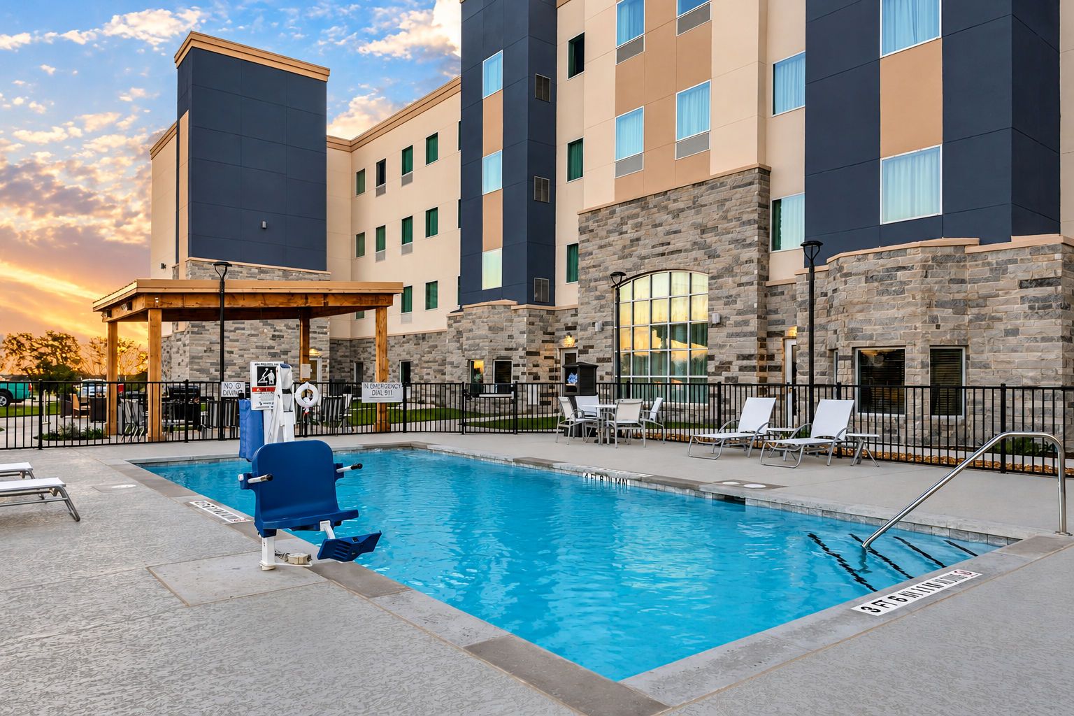 A swimming pool with a lifeguard stand, lounge chairs, and a stone building with multiple windows.