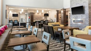 A hotel lobby with a seating area, a kitchen, and a TV mounted on the wall.