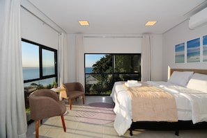 Ein Schlafzimmer mit Bett, Stuhl, Nachttisch und Meerblick.