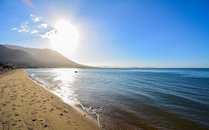 Ein Strand mit Fußabdrücken, ruhigem Wasser und Bergen im Hintergrund.