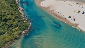 An aerial view of a coastal area with a beach, clear waters, and boats. - Casa com Piscina Vista Mar e Banheira (Palhoça)