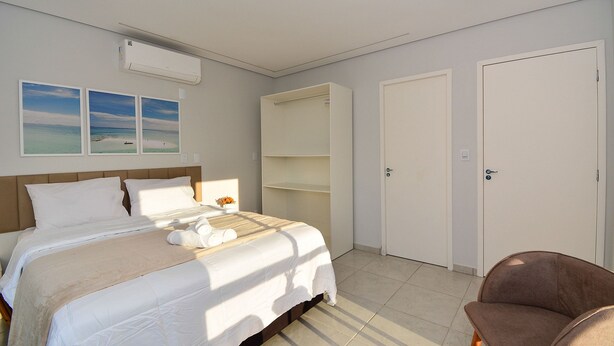 A bedroom with a bed, a chair, a wardrobe, and a door. - Casa com Piscina Vista Mar e Banheira (Palhoça)
