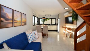 A modern living room with a sofa, dining area, kitchen, and staircase. - Casa com Piscina Vista Mar e Banheira (Palhoça)