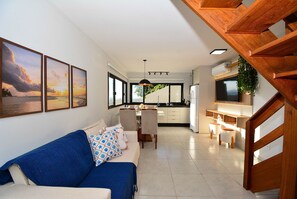 A modern living room with a sofa, dining area, kitchen, and staircase. - Casa com Piscina Vista Mar e Banheira (Palhoça)