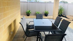 An outdoor patio with a table and chairs, potted plants, and a brick wall. - Busselton Stylish 5 Bed, 3 Bathroom Home (Busselton)