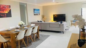 A modern living room with a sofa, TV, dining table with chairs, and artwork on the walls. - Busselton Stylish 5 Bed, 3 Bathroom Home (Busselton)