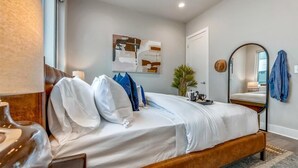 Un dormitorio con cama, espejo, cuadro y puerta.
