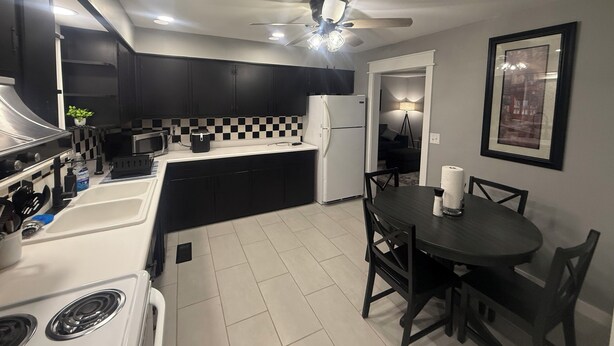 Cocina compacta con estufa, microondas y refrigerador, una mesa de comedor con sillas y un ventilador de techo.