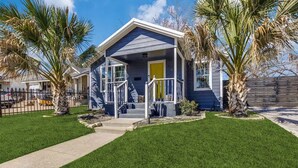 Einbungalow mit einer Veranda, einer gelben Tür und einem kleinen Vorgarten mit Palmen.