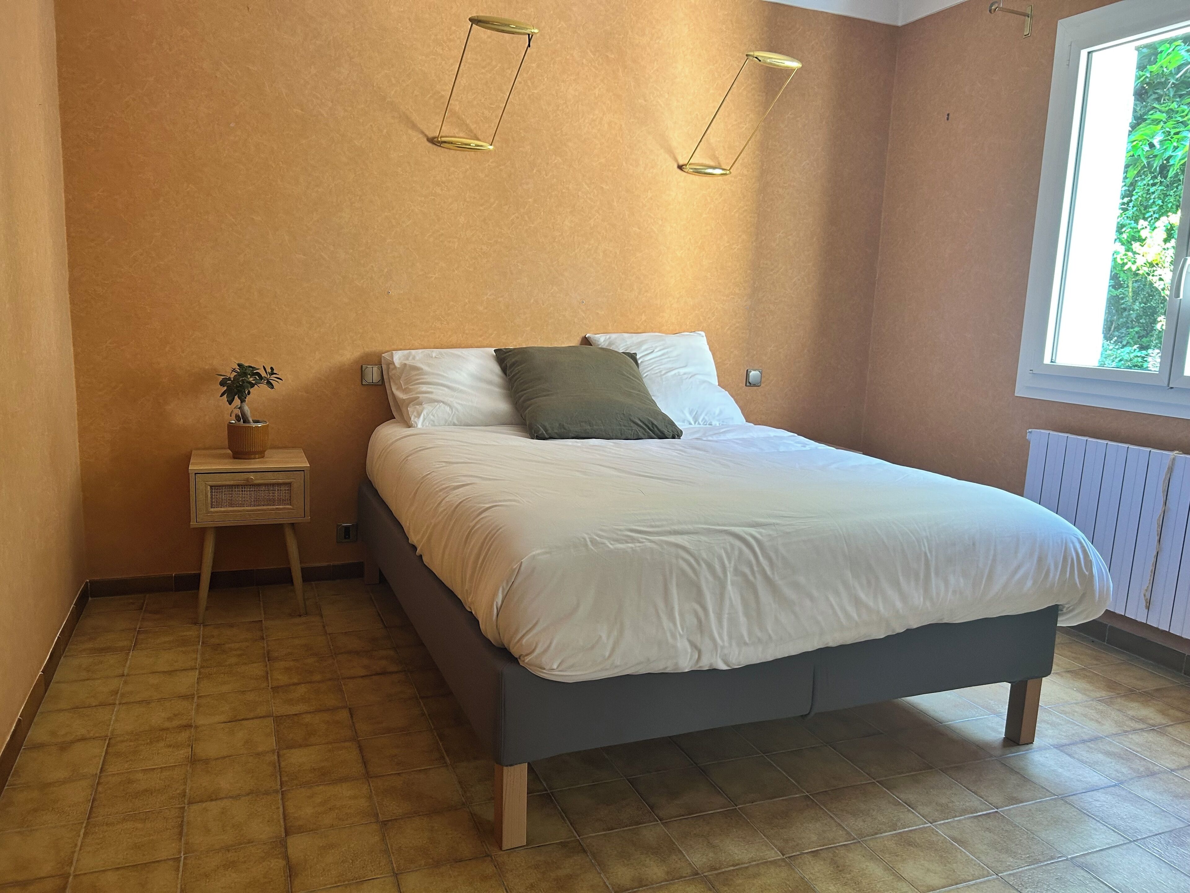 Une chambre à coucher avec un lit, une table de chevet, une lampe et une fenêtre.