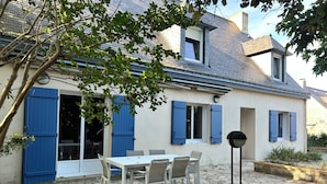 Ein Haus mit einer Steinterrasse, einem Esstisch mit Stühlen und blauen Fensterläden.