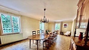 Ein Esszimmer mit großem Tisch, Stühlen, einer Chandelierleuchtre und Blick auf Grünflächen im Freien.