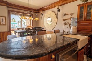 A kitchen with a large island, wooden cabinets, a water dispenser, and a view of the outdoors. - Experience Luxury by the Sea – Condo 16 at Oceans 23, Belize (San Pedro)