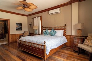 A bedroom with a wooden bed, a ceiling fan, an air conditioning unit, a chair, and a lamp. - Experience Luxury by the Sea – Condo 16 at Oceans 23, Belize (San Pedro)