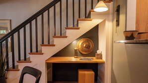 Una escalera con peldaños de madera y barandas negras, una mesa de madera con un cuenco y una vela, y una silla.
