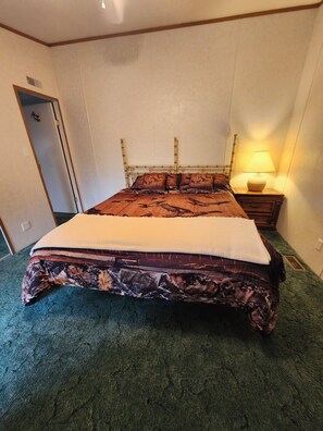 A bed with a patterned bedspread, a bedside lamp, and a green carpet.