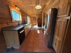A wooden cabin kitchen with a central island, stainless steel appliances, and a hanging light fixture.