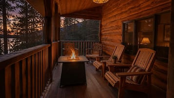 Une terrasse en bois avec un foyer, des sièges et une vue sur les arbres.