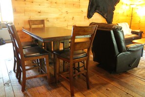 A wooden dining table with four chairs, a leather sofa, and a lamp in a room with wooden flooring.