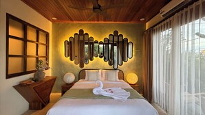 A bedroom with a large bed, a ceiling fan, a wall-mounted mirror, and a window with sheer curtains.