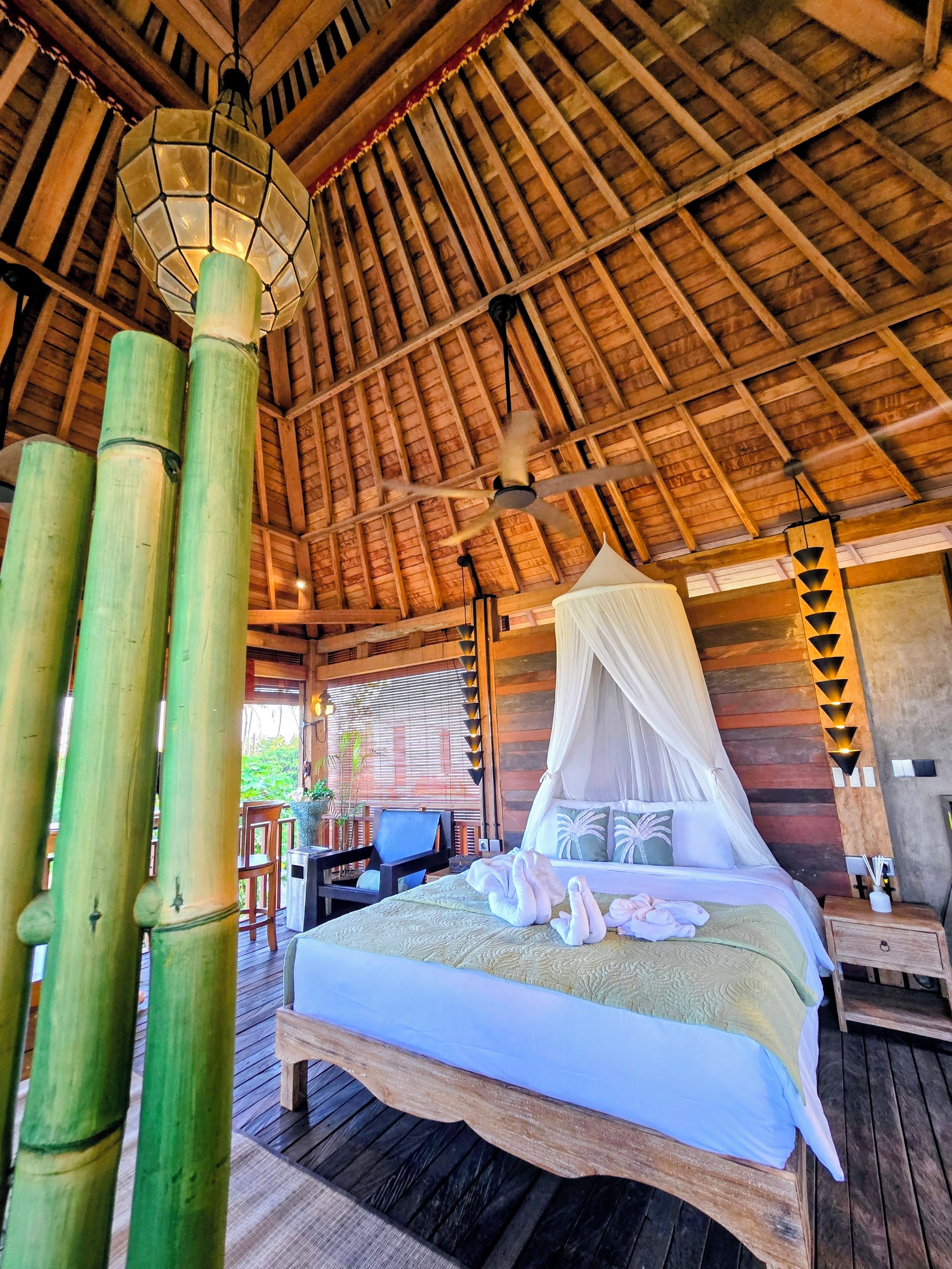 A room with a bed, a ceiling fan, and a large window.