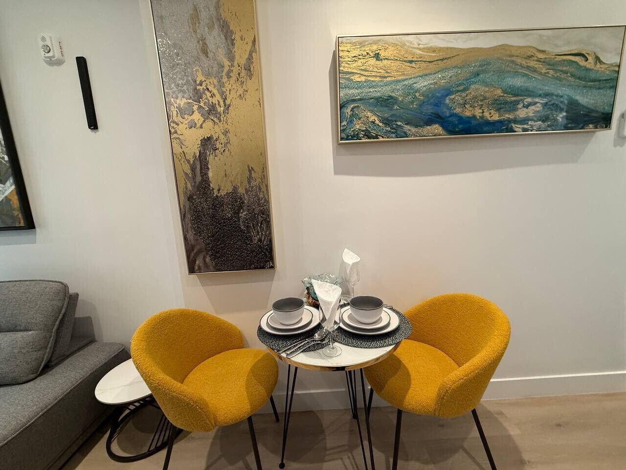 A dining area with two yellow chairs, a small round table, and a painting on the wall.
