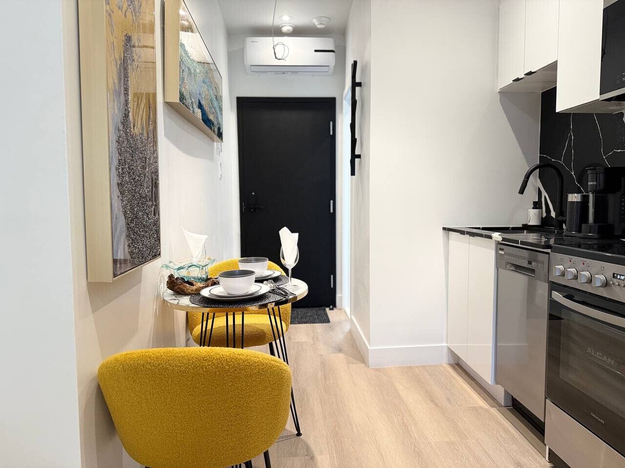 A modern kitchen with a black stove, white cabinets, and a dining area with yellow chairs.