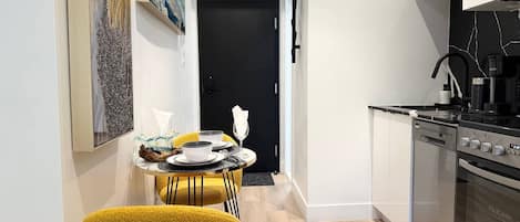 A modern kitchen with a black stove, white cabinets, and a dining area with yellow chairs.