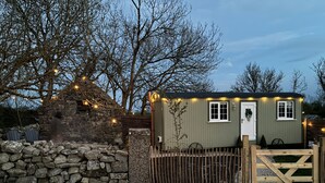 A small, single-story building with a stone wall, a wooden gate, and string lights.