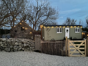 A small, single-story building with a stone wall, a wooden gate, and string lights.