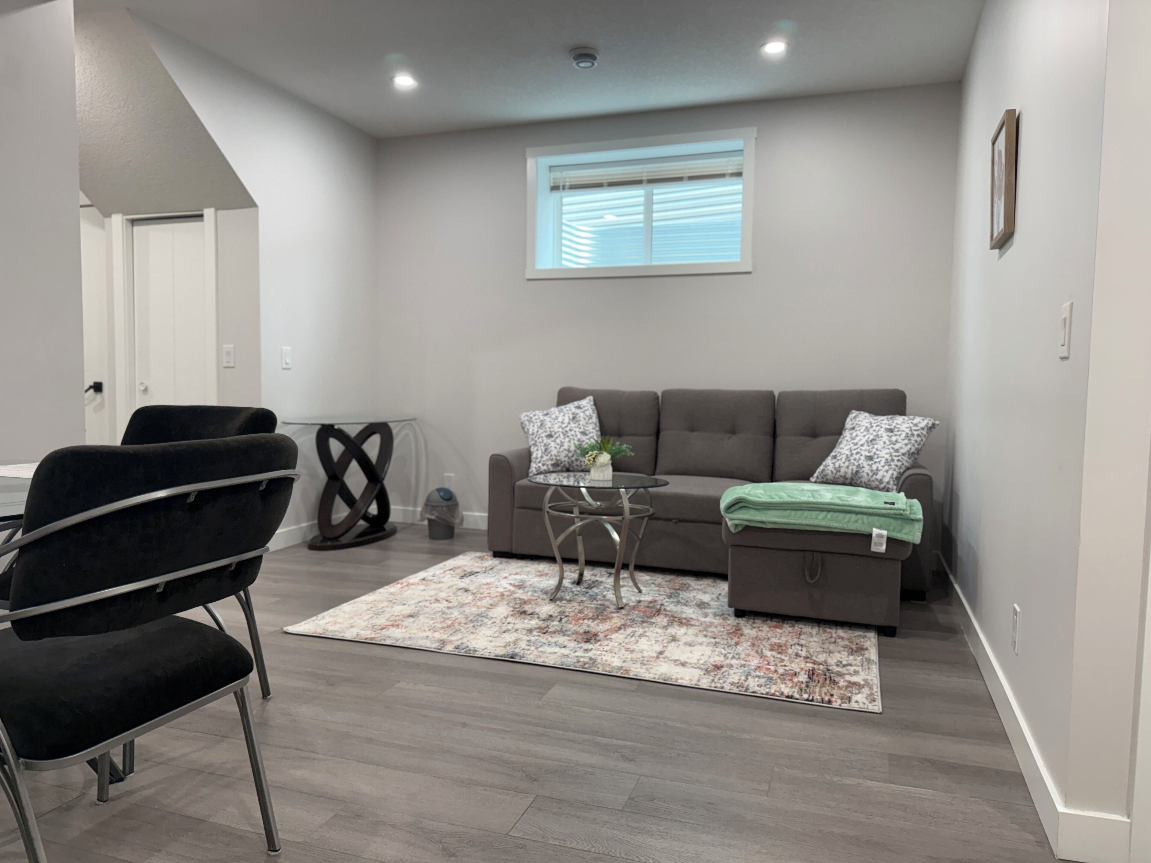 A modern living room with a grey sofa, a black chair, a small table, and a patterned rug.