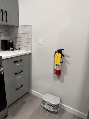 A kitchen with a toaster, a fire extinguisher, and a trash bin. - Cozy legal suite for short-term rental (Calgary)