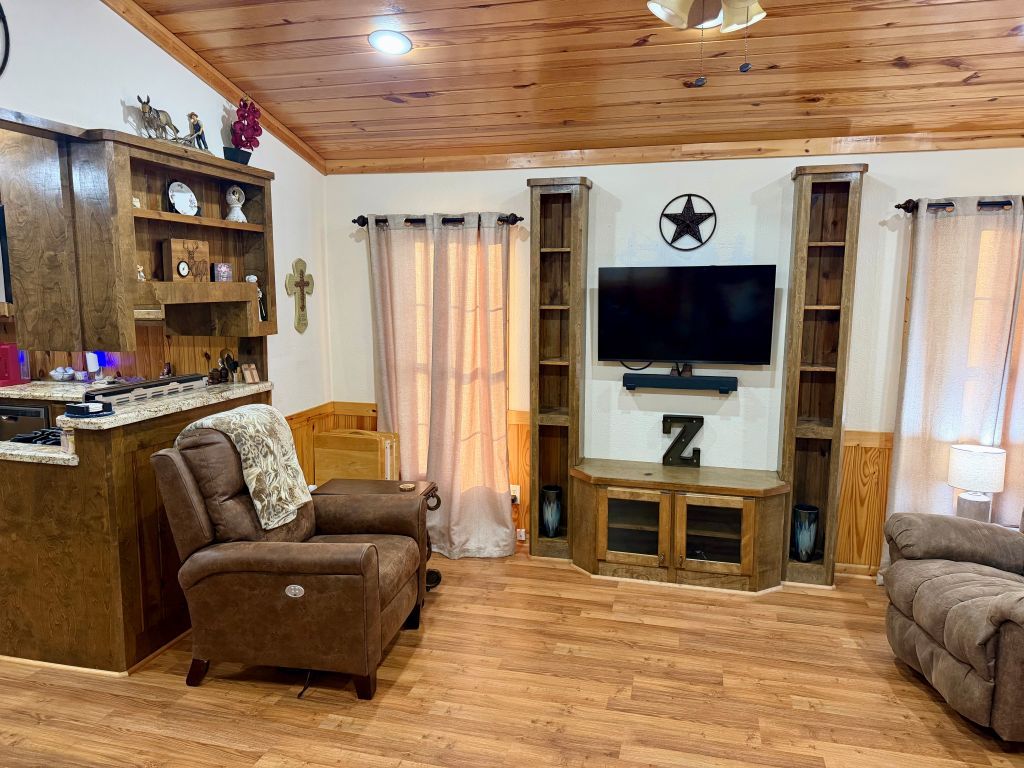 A living room with a wooden ceiling, a flat-screen TV mounted on a wall, a sofa, and a wooden cabinet with shelves.