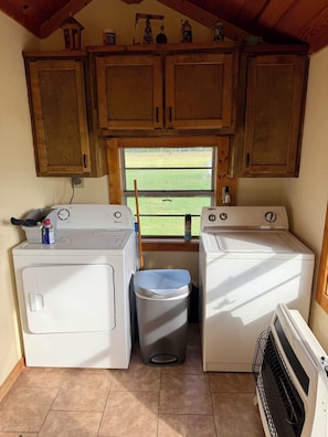 A compact laundry room with two washing machines, a drying machine, and a trash bin.