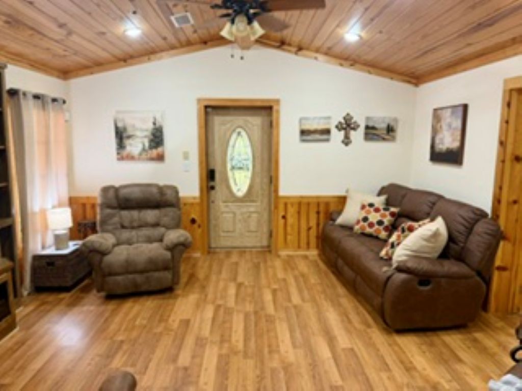 A room with a wooden ceiling, a door with a glass panel, a brown sofa with patterned cushions, and a brown armchair.
