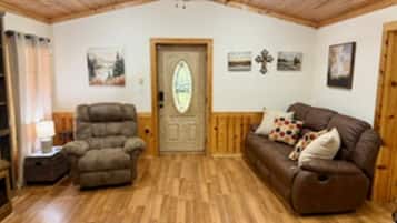 A room with a wooden ceiling, a door with a glass panel, a brown sofa with patterned cushions, and a brown armchair.