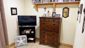 A room with a television on a stand, a wooden dresser with drawers, a fan, and a shelf with framed photos. - Charming 2-bedroom country house 15 minutes from Bryan with AC/Heat. (Bryan)