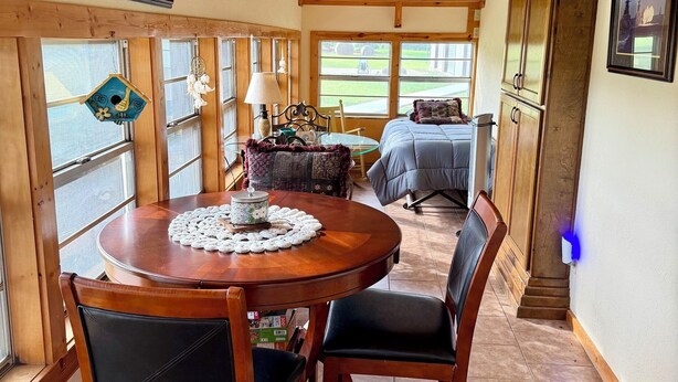A room with a wooden ceiling, a dining table with chairs, a bed, and a window with a view. - Charming 2-bedroom country house 15 minutes from Bryan with AC/Heat. (Bryan)